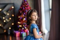 Girl with dark hair standing on a box with gifts. Christmas tree in the background. smiles Royalty Free Stock Photo