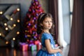 Girl with dark hair standing on a box with gifts. Christmas tree in the background. smiles Royalty Free Stock Photo