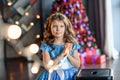 Girl with dark hair standing on a box with gifts. Christmas tree in the background. smiles Royalty Free Stock Photo