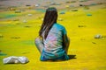 Girl decorated with colorful colors on a Hindi holiday sits on the road strewn with rubbish.