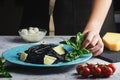 A girl decorates a dish of black spaghetti with basil leaves. Unusual cuttlefish ink pasta. A wholesome light dinner Royalty Free Stock Photo