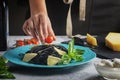 A girl decorates a dish of black spaghetti with cherry tomatoes. Unusual cuttlefish ink pasta. A wholesome light dinner Royalty Free Stock Photo