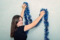 The girl decorates the wall with a blue tinsel, turns around and smiles