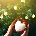 Girl is decorating christmas tree with lights. Present box with toys in woman`s hands. White fluffy heart. Love and holidays Royalty Free Stock Photo