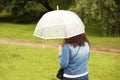 A girl in a denim blue jacket with a white transparent umbrella walks in the rain among the green. Romantic mood. Melancholic wet