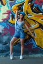 Girl in denim overalls posing against wall with graffiti