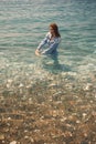 A girl in a waist-length denim jumpsuit stands in seawater half-turned to the camera Royalty Free Stock Photo