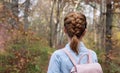 Girl in a denim shirt with a backpack on the background of the autumn forest. Back view of woman with scythe