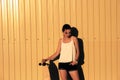 Girl in denim shorts and tank top standing with skateboard in front of yellow mwtal fence and looking down Royalty Free Stock Photo