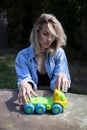 A girl in a denim suit sits on a bench at a table outside in the garden and rolls a small toy car.