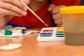 A girl dips a brush in paint of the desired color while painting a craft from salt dough, close-up
