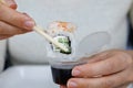 A girl dips a Japanese roll into a box of soy sauce