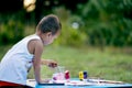 Girl with dirty hands and fingers, using paintbrush painting on paper and her Tank top