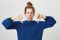 Girl disagree and shows her condemn. Studio shot of displeased frowning redhead european girl in bun and winter sweater Royalty Free Stock Photo