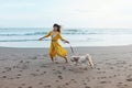 Girl With Dog On Beach. Running Woman In Maxi Yellow Boho Dress Enjoying Summer Vacation With Pet Near Ocean