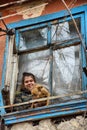 A girl with a dog in a poor quarter looking out the window of an old house Royalty Free Stock Photo