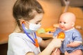 A girl with a doll plays doctor, a nurse listens to the baby through a stethoscope. Pediatrics, vaccination calendar, profession Royalty Free Stock Photo