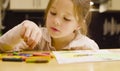 A girl drawing pastel crayons on paper at a table