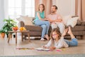Girl draws with colored pencils lying on the floor of house. Happy parents are sitting in background Royalty Free Stock Photo