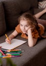 The girl draws while lying on the couch in the living room. The child spends her free time drawing. Royalty Free Stock Photo