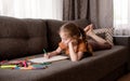 The girl draws while lying on the couch in the living room. The child spends her free time drawing. Royalty Free Stock Photo