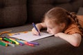 The girl draws while lying on the couch in the living room. The child spends her free time drawing. Royalty Free Stock Photo