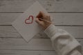 A girl draws a red heart on white paper. The girl draws on a wooden white table Royalty Free Stock Photo