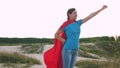 Girl dreams of becoming a superhero. beautiful girl superhero standing on the field in a red cloak, cloak fluttering in