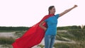 Girl dreams of becoming a superhero. beautiful girl superhero standing on the field in a red cloak, cloak fluttering in