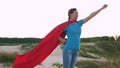 Girl dreams of becoming a superhero. beautiful girl superhero standing on the field in a red cloak, cloak fluttering in