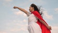 Girl dreams of becoming a superhero. beautiful superhero girl standing on a field in a red cloak, cloak fluttering in