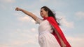 Girl dreams of becoming a superhero. beautiful superhero girl standing on a field in a red cloak, cloak fluttering in