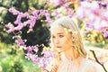 Girl on dreamy face, tender blonde near violet flowers of judas tree, nature background. Young woman enjoy flowers in