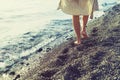 Girl in a dress with bare feet walks along a pebble beach along the sea at sunset. Royalty Free Stock Photo