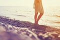 Girl in a dress with bare feet walks along a pebble beach along the sea at sunset. Royalty Free Stock Photo