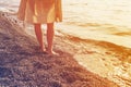Girl in a dress with bare feet walks along a pebble beach along the sea at sunset. Royalty Free Stock Photo