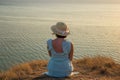 A girl in a dress and hat sits on a cliff by the sea Royalty Free Stock Photo