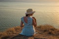 A girl in a dress and hat sits on a cliff by the sea Royalty Free Stock Photo