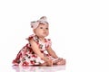 Baby girl in a dress and headband bow sitting barefoot on a white background Royalty Free Stock Photo