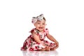 Baby girl in a dress and headband bow sitting barefoot on a white background. Royalty Free Stock Photo