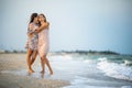 A girl in a dress hugs her mom in a dress while walking along the beach near the sea with waves Royalty Free Stock Photo