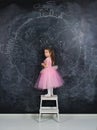 Girl in dress stands on a chair near a big chalkboard Royalty Free Stock Photo