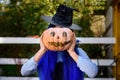 A girl dressed as a witch covered her face with a pumpkin with an evil face drawn in the style of a Halloween celebration