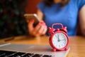 A girl dressed in a blue dress works in a smartphone in the foreground a red clock. Concept dead line