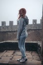 A girl dressed in a denim jacket and blue pants, posing against the backdrop of a medieval fortification. travel and fashion Royalty Free Stock Photo