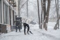 A girl dressed in light winter clothes is shoveling snow off the walkway. Behind her is a man with a shovel.