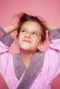 A girl dressed in a terry bathrobe straightens her hair