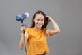 Girl dries hair with a hairdryer on a gray background, having fun