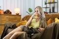 A girl is drinking hot tea from a kuka and looking into the distance. The dog lies bored on the sofa. A multi-racial dog