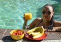 Girl drinking orange juice and eating fruits in the pool